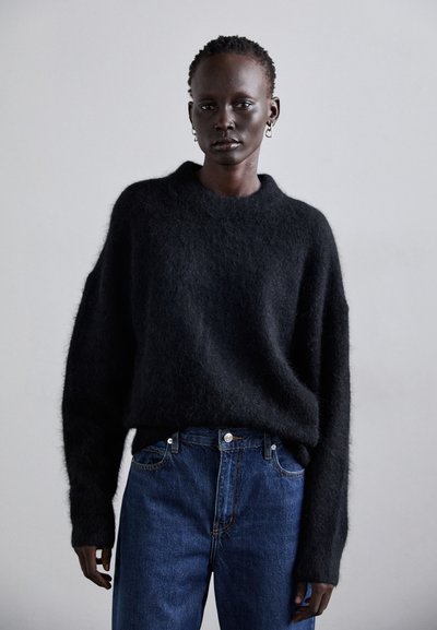 Pull en maille noir avec une coupe décontractée et un col rond, associé à un jean en denim bleu foncé avec poches avant et couture claire.
