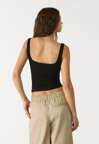 Black fitted tank top with wide shoulder straps, featuring a square back design, paired with khaki relaxed pants with an elastic waistband.