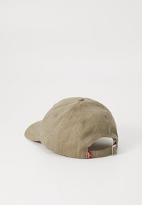 Brun herringbone-mønster caps med en buet skjerm, justerbart reim bak og liten rød etikett på siden. Strukturert form og teksturert stoff.