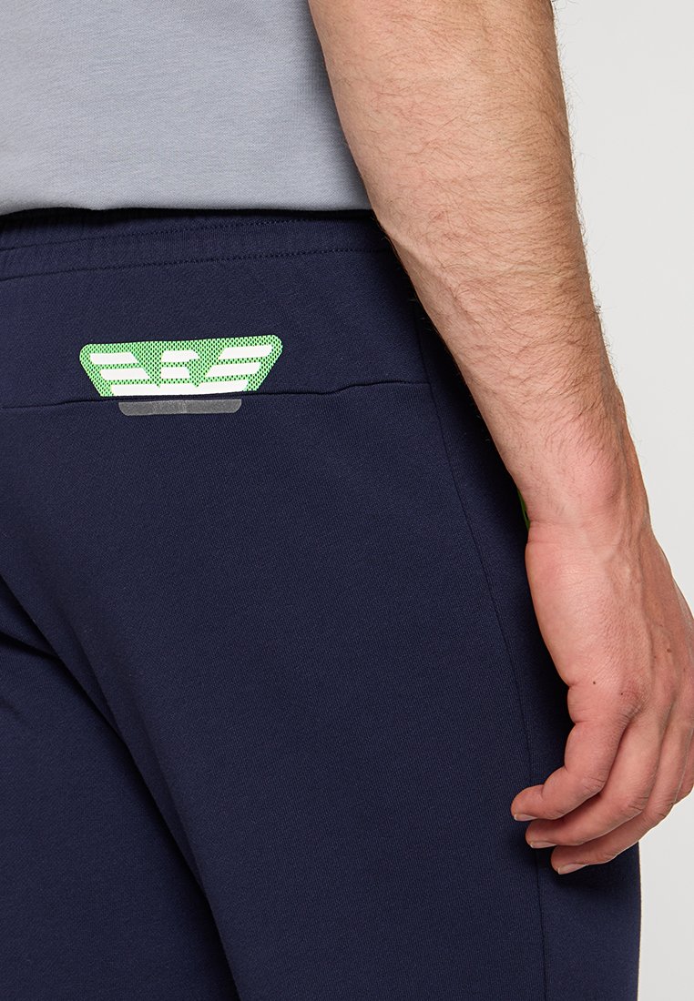 Granatowe spodnie sportowe z teksturowanym pasem, z zielonym i białym logo na tylnej kieszeni. Miękki, elastyczny materiał.