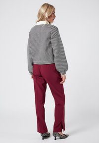 Svart och vit mönstrad kortärmad tröja med ballongsärmar, kombinerad med bordeauxfärgade byxor med sidokläppar och svarta texturerade klackar.