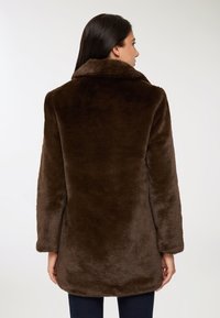 Brązowy płaszcz z sztucznego futra o miękkiej teksturze, z dużym kołnierzem i luźnym krojem. Płaszczyk ma długie rękawy i sięga do połowy uda.