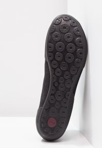 Black sneaker with a textured fabric upper and a rubber outsole featuring circular patterns for traction. Simple, minimalist design.