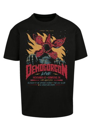 Czarny bawełniany t-shirt z wyraźnym czerwono-żółtym wzorem graficznym przedstawiającym Demogorgona, z informacjami o wydarzeniu w niebieskim i czerwonym tekście.