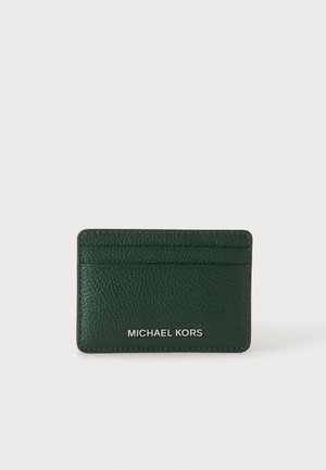 Tarjetero de cuero texturizado color verde oscuro con tres ranuras para tarjetas y logo plateado de Michael Kors en la parte frontal sobre un fondo liso.