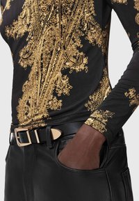 Must mustriga mustriga top kuldsete keerukate mustritega; koos mustade nahkpükstega, mis on varustatud struktureeritud vöö ja ainulaadse kuldse klambriga.