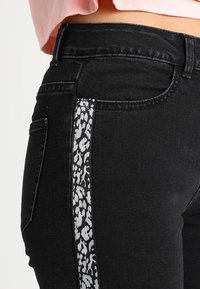 Jeans de mezclilla negros con un diseño ajustado, que presentan una franja de estampado de leopardo blanco a lo largo del lateral y bolsillos estándar.