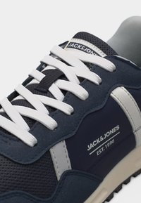 Baskets bleu marine avec lacets blancs, bande latérale blanche, et logo "JACK & JONES EST. 1990" sur le côté et la languette.