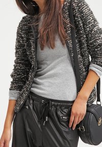 Svart och grått texturerat cardigan med dragkedja, lagd över en grå tröja. Kombinerad med svarta fusklederbyxor och en rund handväska.