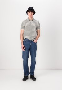 Šedý a biely pruhovaný polo tričko v kombinácii s modrými džínami. Model nosí čierny klobúk a čierne tenisky. Jednoduchý, neformálny outfit.