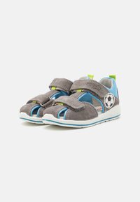 Graue Wildleder-Sandalen mit blauen Akzenten, offenes Zehendesign, zwei verstellbare Klettverschlüsse und ein Fußball-Emblem an der Seite.