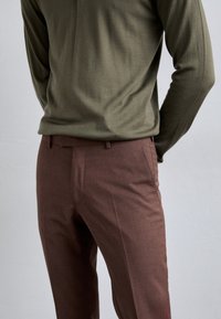 Braune maßgeschneiderte Hose mit flachem Frontschnitt und schmaler Passform, kombiniert mit einem langen, olivgrünen Hemd aus weichem, strukturiertem Stoff.