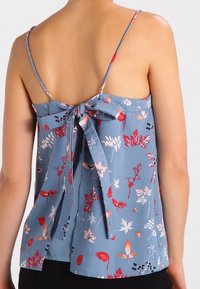 Ljusblå ärmlös topp med en knytbakdesign, prydd med blommiga mönster i röd, rosa och vitt på en silkeslen yta.