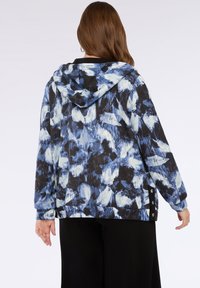 Giacca con cappuccio caratterizzata da un motivo astratto blu e nero, tessuto morbido, vestibilità ampia e dettagli con bottoni a scatto sui lati.