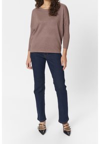 Maglione a maglia marrone chiaro con maniche a tre quarti, abbinato a jeans blu scuro e tacchi a punta neri con dettagli a strappo.