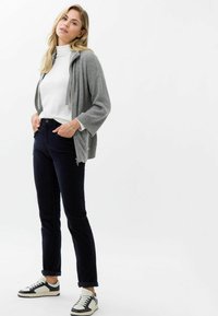 Grijze geribbelde cardigan met banden, witte coltrui, donkerblauwe broek en zwart-witte sneakers. Getailleerde silhoutte met een casual ontwerp.