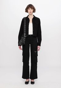 Giacca nera a bolero sopra una maglietta bianca, abbinata a pantaloni cargo neri a vita alta con tasche e zip. Includono ballerine nere e borsa.