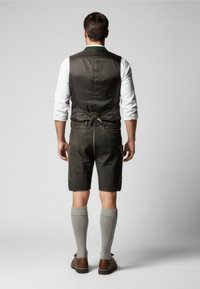 Dark leather shorts with yellow stitching, grey knitted knee socks, brown shoes, and a dark vest over a white shirt.