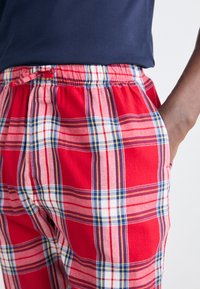 Rød ternet pyjamasbukser med elastisk talje, prydet med blå og hvide striber, blødt stof og sidelommer.