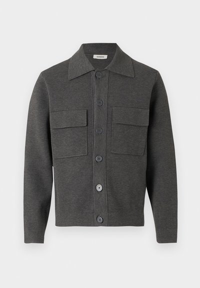 Σκούρο γκρι μπουφάν με κουμπιά μπροστά, μυτερό γιακά και δύο μεγάλες τσέπες με καπάκι στο στήθος, κατασκευασμένο από πλεκτό ύφασμα.