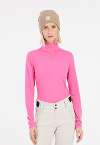 Maglia a maniche lunghe rosa con zip a un quarto, realizzata in materiale leggero. Abbinata a pantaloni chiari con tasche laterali con zip.