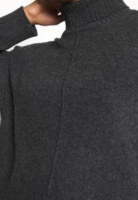 Suéter gris de punto con cuello alto y tela texturizada. Presenta un diseño limpio sin patrones ni acentos adicionales.