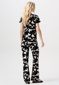 Černá a béžová souprava pohodlného oblečení s květinovým potiskem, zahrnující vršek s krátkým rukávem a zvonové kalhoty vyrobené z měkké, lehké tkaniny.