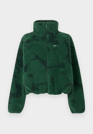 Veste en polaire verte raccourcie avec une surface texturée, col montant, fermeture éclair frontale, et imprimé discret. Présente un petit logo blanc sur la poitrine.