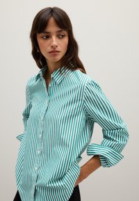 Camicia a righe verdi e bianche con colletto, maniche arrotolate e una vestibilità rilassata, realizzata in tessuto leggero.