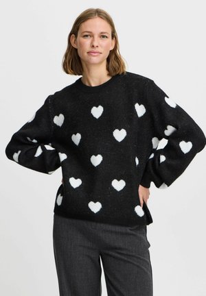 Maglione nero realizzato in tessuto testurizzato, con motivi a cuore bianchi su tutta la superficie. Collo rotondo e vestibilità ampia con spalle scese.