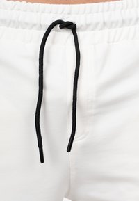 Pantaloni sportivi bianchi con cordino nero. La vita è elastica e il tessuto sembra liscio ed elastico, con dettagli di cucitura.