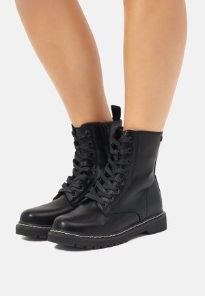 Botines de cuero negro hasta el tobillo con un cierre de cordones en la parte frontal, cremallera lateral, suela texturizada y detalle de costura en contraste. Acabado suave y diseño robusto.