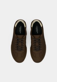 Brown suede sneakers with contrasting cream accents, featuring round toe, lace-up design, and textured surface. Brand name visible inside.