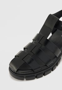 Svarte lær sandaler med et vevd stroppdesign. Kraftig såle med en teksturert overflate og en lett glans. Åpen tå-stil.