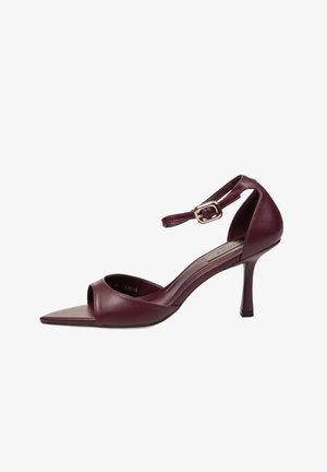 Sandalia de tacón alto de cuero burdeos con punta puntiaguda, correa en el tobillo y hebilla dorada sobre fondo blanco.
