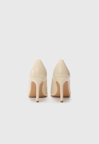 Scarpe con tacco alto in pelle beige con punta affusolata e tacco stiletto sottile, caratterizzate da una superficie liscia e un design minimalista.