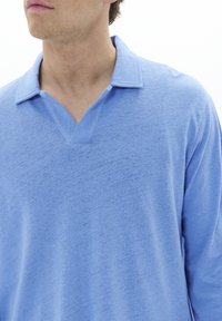 Light blue polo shirt with a textured finish, featuring a v-neck and a standard collar. The fabric appears soft and casual.