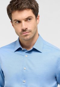 Camicia azzurro chiaro con colletto che presenta un motivo floreale all'interno. Realizzata in un tessuto morbido, con una leggera texture.