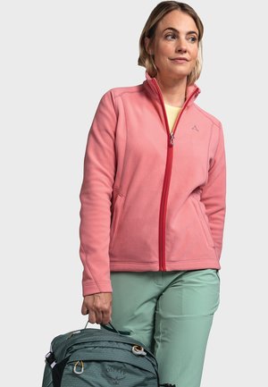 Fleecejacke in Hellrosa mit einem roten Reißverschluss, Seitentaschen und hohem Kragen, kombiniert mit hellgrünen Hosen und einem grünen Rucksack.