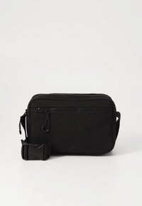 Bolso bandolera negro hecho de tela duradera, con un compartimento principal con cremallera, correa ajustable y un pequeño bolsillo delantero.