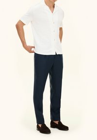 Camicia bianca a maniche corte con motivo testurizzato e bottoni in legno, abbinata a pantaloni blu scuro e scarpe mocassino marroni. Design semplice e classico.