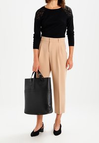 Bolso tote de cuero negro con asas dobles, textura suave y un diseño minimalista. Combinado con pantalones beige ajustados y una blusa negra de mangas de encaje.