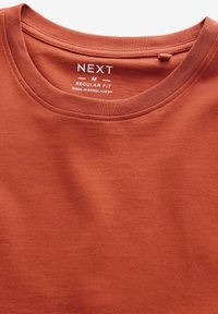 Rostrød crew neck t-shirt lavet af blød bomuld. Har en normal pasform og inkluderer et mærke, der angiver størrelse og plejeoplysninger.