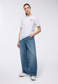 T-shirt di cotone bianco con testo grafico rosa "FRESH UP", abbinato a jeans in denim blu a gamba larga e scarpe da ginnastica bianche. Design semplice e casual.