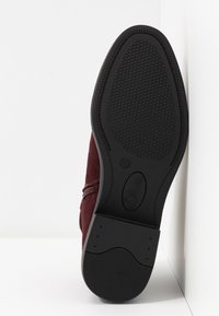 Chaussure en daim bordeaux avec une semelle extérieure en caoutchouc noir texturée. Elle est dotée d'une fermeture éclair latérale et de détails de coutures discrètes le long du bord supérieur.