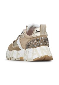 Sneakers har en överdel i beige mocka och tyg med silverdetaljer, en kraftig vit och tan sula, samt dekorativa metallnitar på hälen.