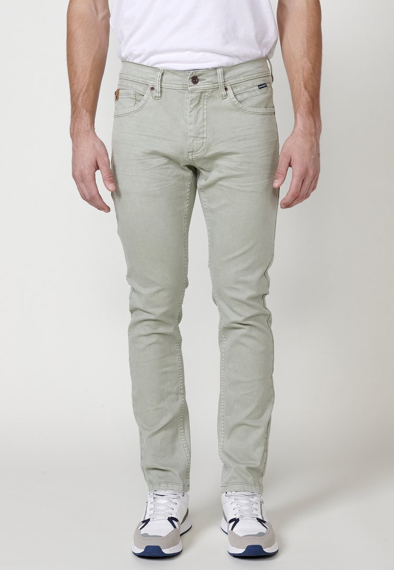 Jeans verde claro con un corte slim, diseño de cinco bolsillos y cierre de botón. La tela tiene una textura suave con un ligero desgaste.
