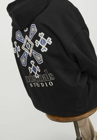 Czarny hoodie z misternym białym, niebieskim i jasnoniebieskim haftem z tyłu, z białym napisem "originals STUDIO".