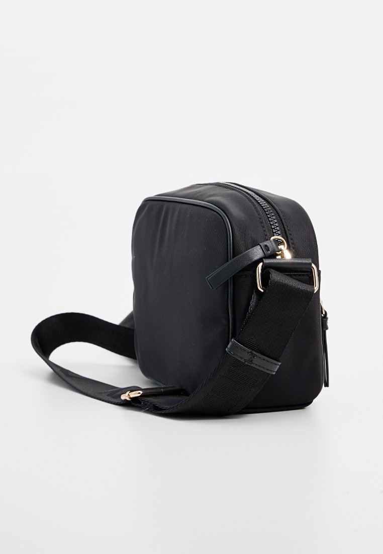 Bolso bandolera negro de nailon con forma rectangular, cierre de cremallera, correa ajustable y acentos de hardware en tono dorado.