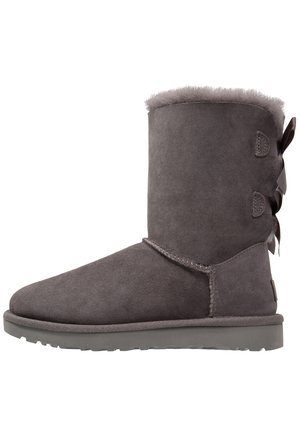 Grau Wildleder-Ankle-Boot mit einem weichen Futter aus Fell, runder Zehenform, flacher Sohle und dekorativen Schleifen auf der Rückseite.